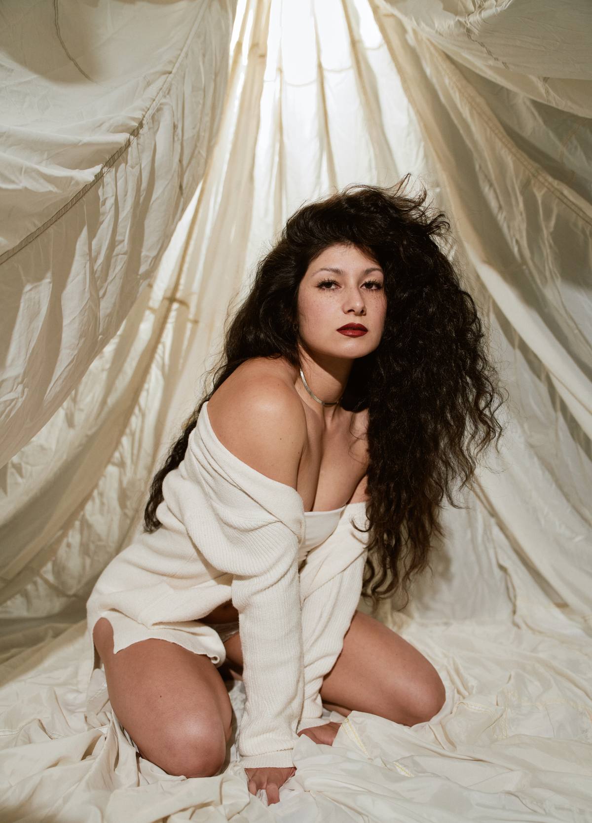 Ruby kneeling in a cream outfit among draped fabric